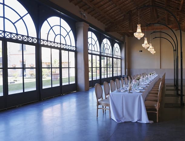 Long table set in front of arched windows, beneath the chandeliers