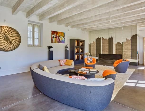 Living room under pale beams with a curved sofa and a wall sculpture