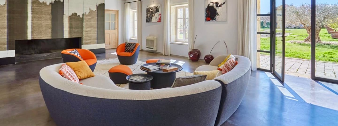 Living room with a curved sofa and orange armchairs, opening onto the grounds